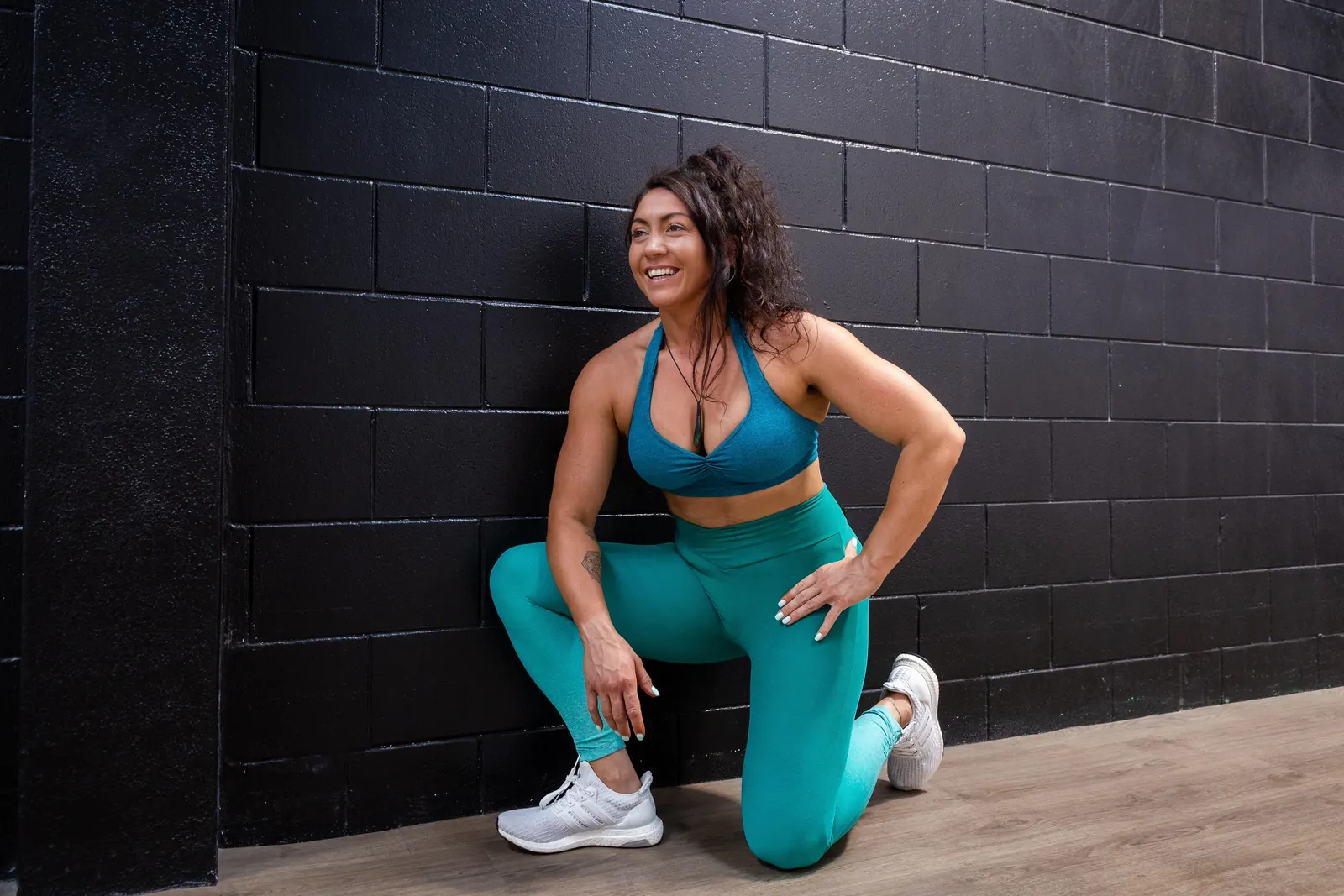 Kiri kneeling against a black brick wall, smiling